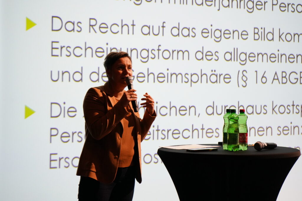 Juristin Christina Forstner auf einer Bühne vor einer Leinwand mit Gesetzestexten.